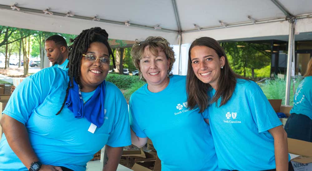 Three women wearing blue cross shirts and smiling