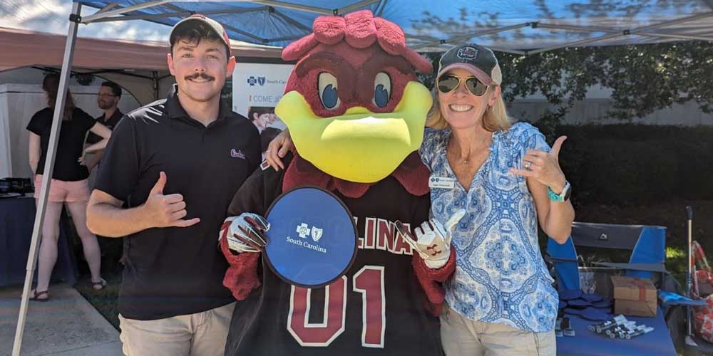 man and woman posing with cocky mascot holding blue cross sign
